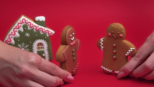 Gay Christmas. Romantic winter holidays. New Year celebration. Female hands with brown gingerbread man cookie couple gathering for party at house kissing isolated on red conceptual background.