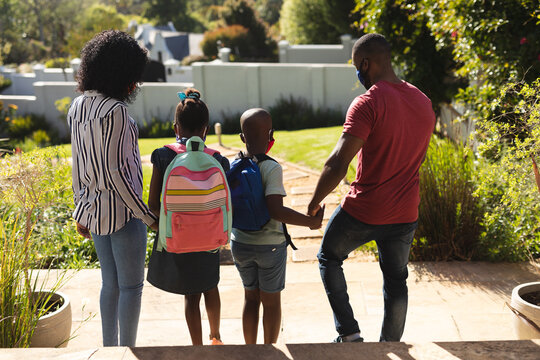 Rear view of african american family wearing face mask standing in the garden holding hands on a bri
