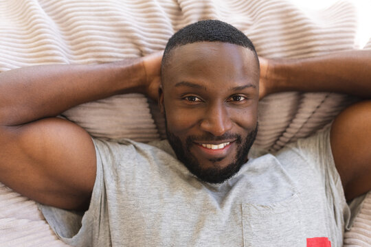 Portrait of  african american man smiling while lying with hands behind his head at home