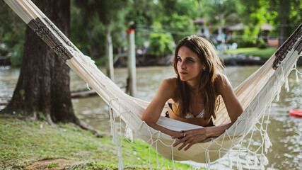 young woman smiling, sitting in the Paraguayan hammock in the forest with river water in the...