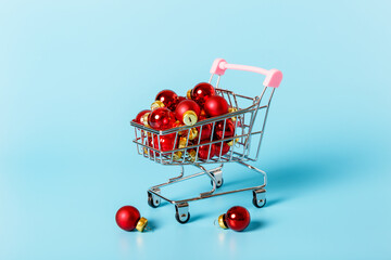 Red christmas balls in a shopping cart on a blue background. Christmas and New Year celebration concept. Holiday shopping and gift shopping concept. Minimalism.