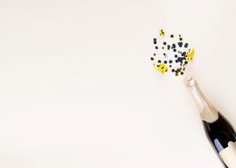 Holiday attributes. Bottle of champagne and confetti in form of splashes for new year on beige background. Top view. Copy space