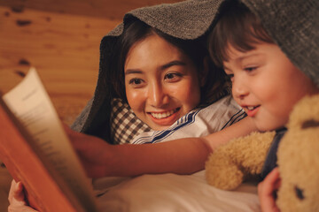 Mother and daughter read bed story book in bedroom at night.