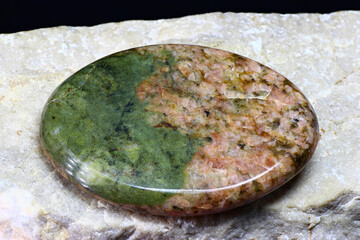 Unakite (granite with green epidote) processed in the form of a cabochon on a white marble background
