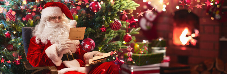 Santa Claus Sitting at His Room at Home Near Christmas Tree and Reading Christmas Letter - obrazy, fototapety, plakaty