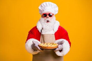 Photo of excited santa claus chef headwear grandpa grey beard hold ready fresh sweet big pie jam masterpiece wear x-mas costume gloves sun specs cap apron isolated yellow color background