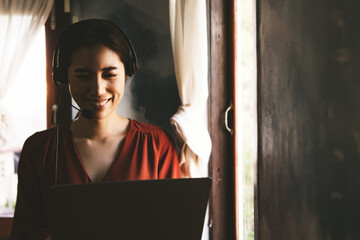 Asian businesswoman wearing a wireless headset working at home with notebook computer, relexing with E-business beside the window