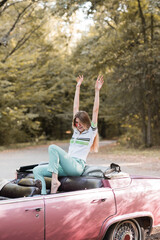 excited barefoot woman sitting in cabriolet with hands in air
