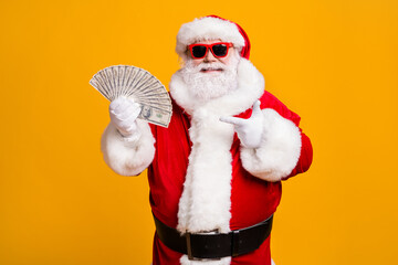 Fototapeta na wymiar Portrait of his he nice attractive cheerful confident fat overweight bearded Santa holding in hand demonstrating usd cash budget isolated bright vivid shine vibrant yellow color background