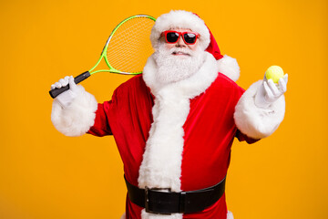 Fototapeta na wymiar Portrait of his he nice attractive cheerful sportive Santa holding in hand tennis ball having fun playing badminton isolated over bright vivid shine vibrant yellow color background