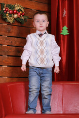 little boy having fun on the couch in the Christmas studio in red. Christmas tree and teddy bear on the background