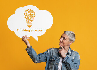 Senior woman holding speech bubble with drawing of light bulb and words THINKING PROCESS on yellow background
