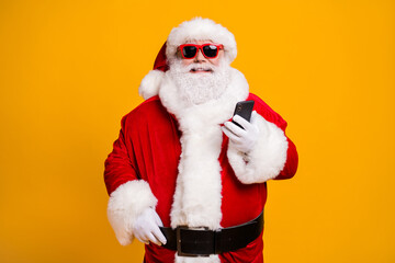 Portrait of his he nice attractive cheerful cheery Santa using device gadget chatting web service shopping order isolated over bright vivid shine vibrant yellow color background