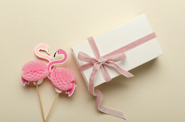 Closeup of two decorative flamingos and white box with pink ribbon on the bright desk