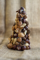 Christmas tree made of autumn ripened brown fruits on jute beige background, chestnuts cones beech nuts almonds walnuts peanuts