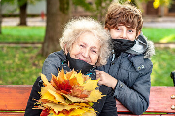 Happy teenager boy in a black mask presented an elderly woman a bouquet of fallen leaves outdoors...