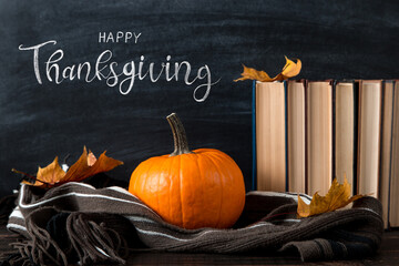 Thanksgiving greetings. Pumpkin and book on a chalkboard background, top view. Kaligraphic capital inscription.