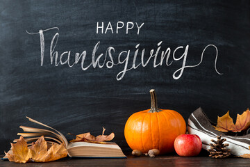 Thanksgiving greetings. Pumpkin, leaves, apples, book, pen on a chalkboard background, top view. Kaligraphic capital inscription.