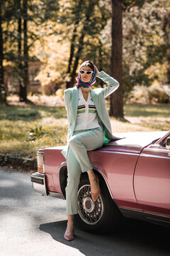 Elegant woman in sunglasses standing near vintage car on road
