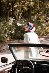 Naklejka premium Woman in headscarf and sunglasses standing near auto on blurred foreground on road