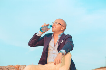man in eyeglasses drinking a water outside sitting on rocks outdoors