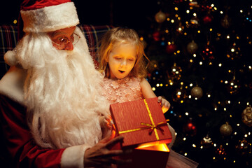 Santa Claus and little girl open a Christmas present Santa gives a child a gift box for the new year