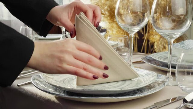 Close up of woman setting table for event. Hands of a housewife or waitress putting cloth napkin on plates