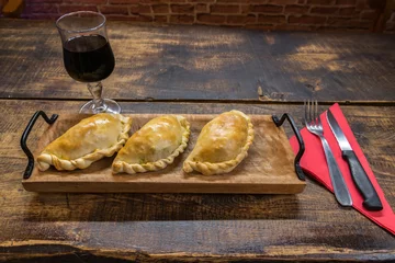 Poster Traditional baked Argentine and Uruguay empanadas savoury pastries with meat beef stuffing against wooden background © martinscphoto
