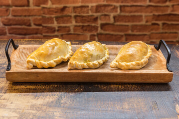 Traditional baked Argentine and Uruguay empanadas savoury pastries with meat beef stuffing against wooden background