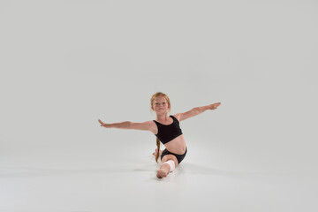 Fototapeta na wymiar Full length shot of little redhead girl, professional gymnast looking away, doing splits, showing flexibility isolated over grey background