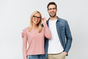 Smiling man in eyeglasses embracing girlfriend isolated on grey