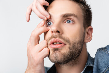 Young man putting contact lens in eye isolated on grey