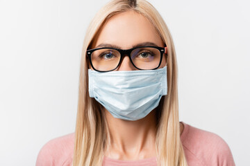Young blonde woman in eyeglasses and medical mask looking at camera isolated on grey