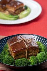 Dong Po Pork meat in a blue plate with broccoli with red background.