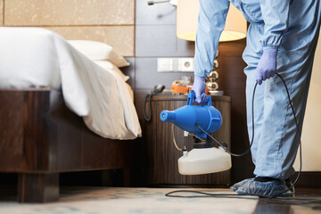 Man in protective overalls cleaning the air from viruses near the bed