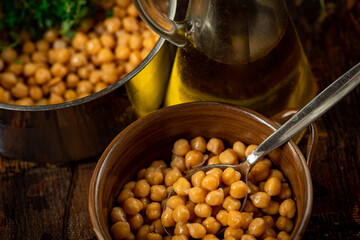 Chickpeas with herb in pot and in bowl with spoon, glass carafe with olive oil.