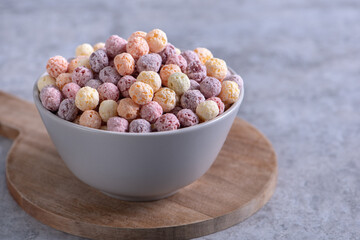 Colorful cereal corn balls mix sweets in a bowl on gray cement background.