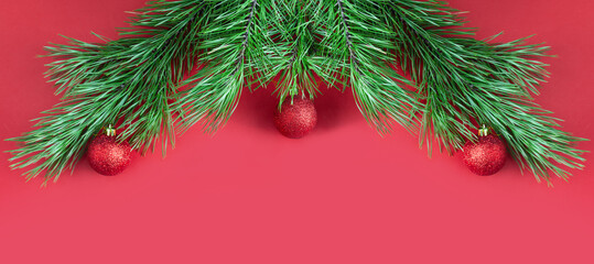 Fototapeta na wymiar Christmas tree branches with red glittering balls on red background with copy space