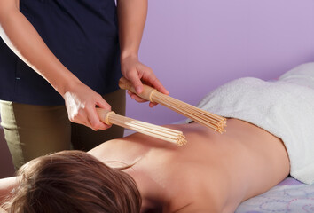 Hands of masseur with bamboo sticks doing massage of back