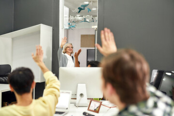 Cheerful aged woman, senior intern waving, saying goodbye to her young colleagues while leaving...