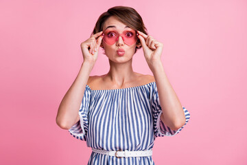 Photo portrait of pouting girl touching rose-tinted heart-shaped glasses isolated on pastel pink colored background
