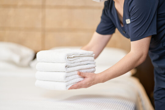 Housemaid keeping bunch of clean towels over bed