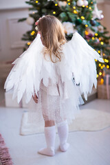child with angel wings by the christmas tree
