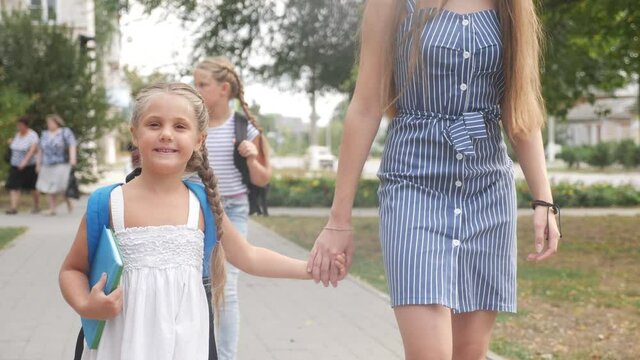 mom and daughter go to school. happy family school education concept. schoolgirl with mom go hand in hand to school on footpath in the park. little girl with a lifestyle briefcase time to study