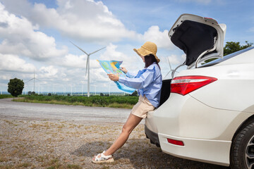 woman in the trunk of a car looking at a map to reach the holiday destination with blue sky and wind turbines background