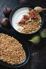 Greek yogurt with granola, sliced figs and honey in a black bowl, studio shot on a dark brown stone background