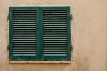 Fototapeta na wymiar window with closed green painted wood shutters, bright wall with space for text, no person