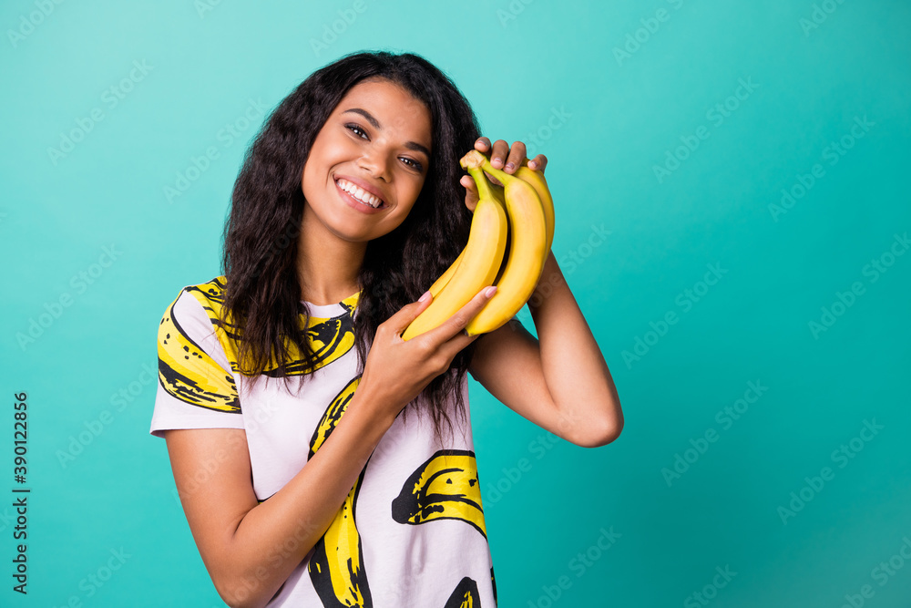 Wall mural photo of cheerful afro american charming girl hold bananas isolated over teal color background