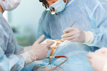 Surgeon and his assistant performing cosmetic surgery on nose in hospital operating room. 