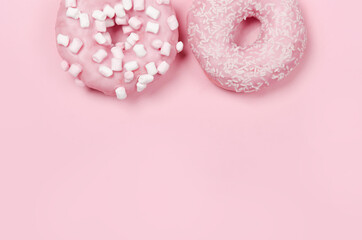 Two donuts with icing on pastel pink background. Copyspace